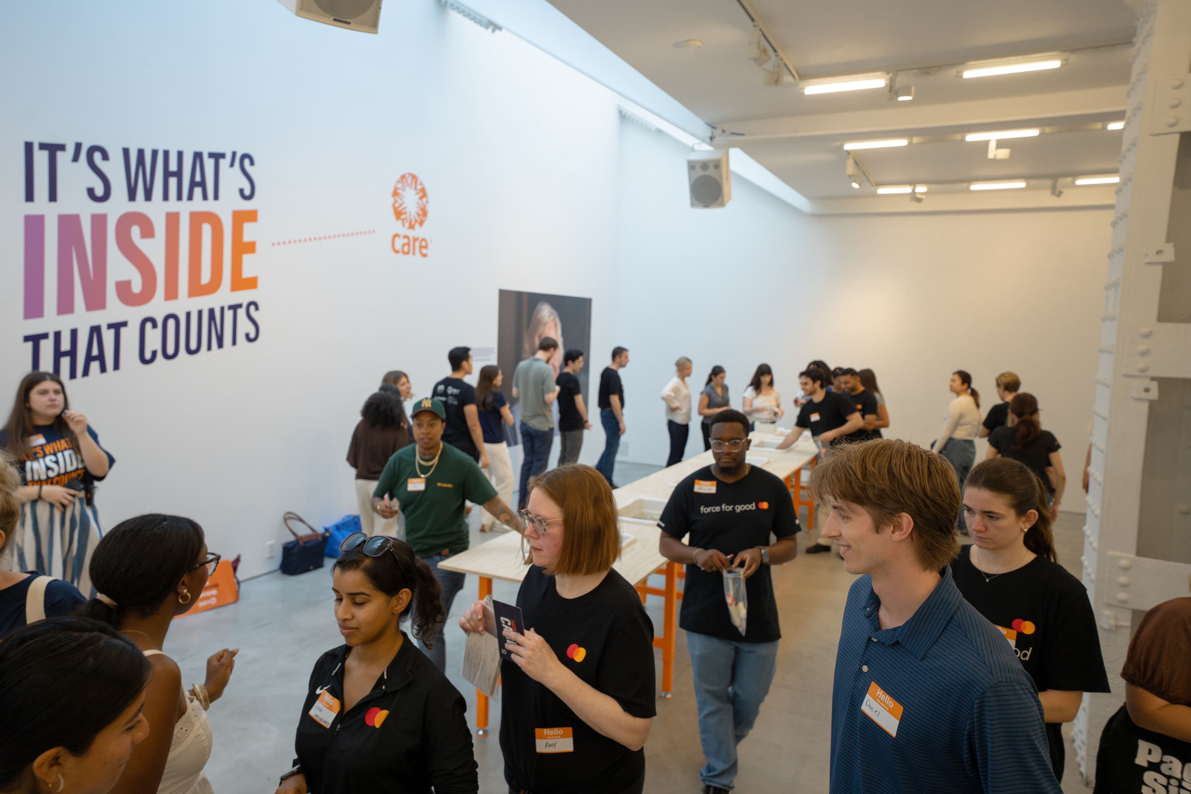 A crowd of attendees and volunteers in Mastercard and CARE branded shirts gathered near the "It's What's Inside That Counts" wall graphic at the pop-up event