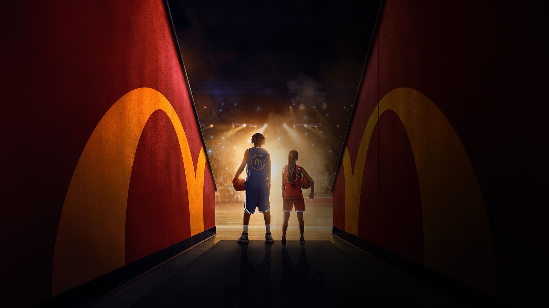 A boy and a younger girl facing about to enter a basketball court in the spotlight of a crowded stadium